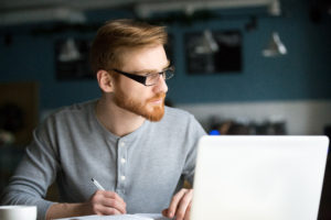 Thoughtful man thinking writing notes in cafe, serious student studying or working in cafeteria, focused pensive writer searching for inspiration muse looking for new creative ideas in public place. Thinking of reputation management plan