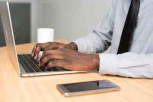 person-wearing-white-dress-shirt-and-black-necktie-using-macbook-air-on-beige-wooden-table