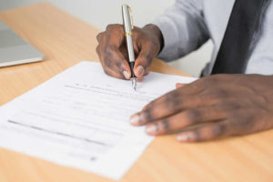 person-holding-gray-twist-pen-and-white-printer-paper-on-brown-wooden-table