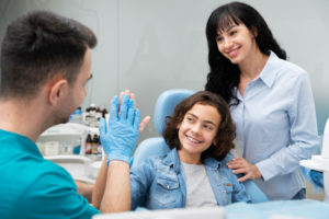 Dentist giving high five to child patient with mother, showing trust and care.